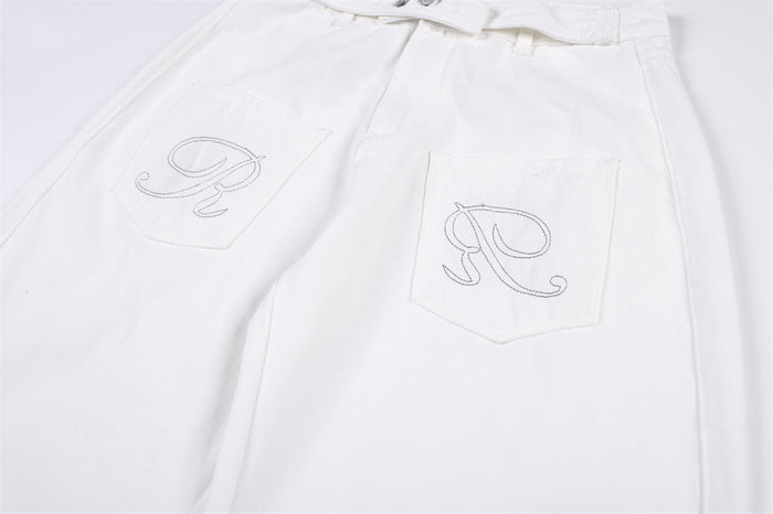 Close-up of white jeans showing two patch pockets with outlined embroidered designs