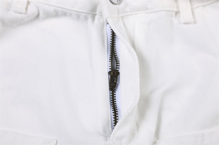 Close-up of the white jeans’ front fly showing a dark metal zipper and stitched waistband
