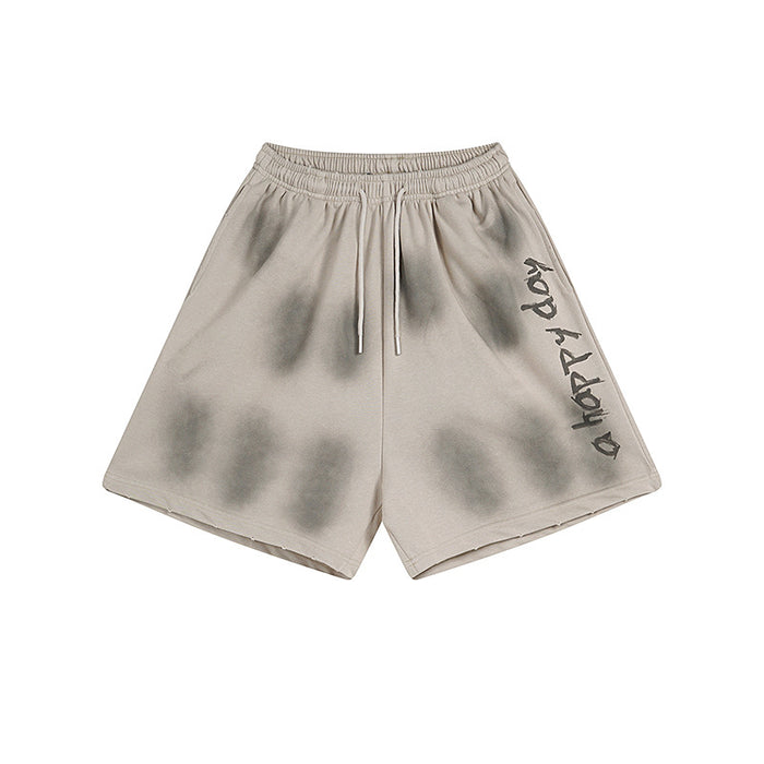 Baggy mens washed sweat shorts in faded beige with spray-shadow print and vertical 'a happy day' graphic on the leg