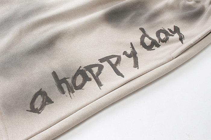 Close-up of beige shorts featuring the dark handwritten-style Happy day graphic near the lower leg