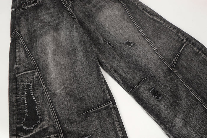 Close-up of washed black denim legs showing distressed holes, panel seams, and a side utility pocket