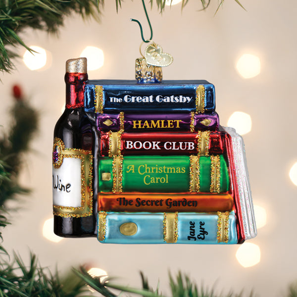 A colorful Christmas tree ornament shaped like a stack of classic books and a bottle of wine, with titles including The Great Gatsby, Hamlet, A Christmas Carol, The Secret Garden, and Jane Eyre.