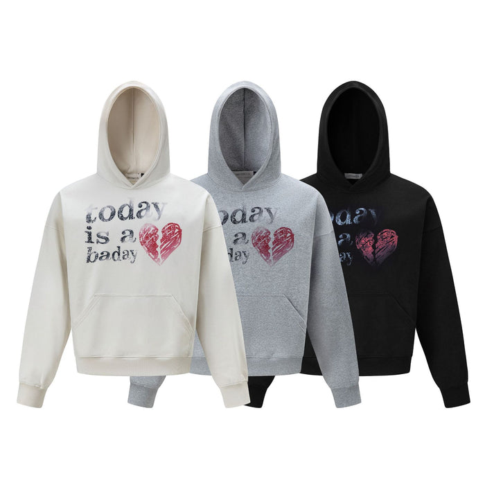 Three oversized graphic hoodies in cream, gray, and black with front text and broken heart prints