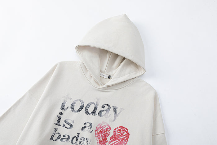 Cream hoodie shown at an angle with its hood, chest graphic, long sleeve, and soft textured fabric