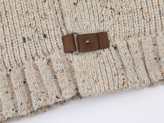 Close-up of a brown leather buckle closure against speckled beige knit above a ribbed edge