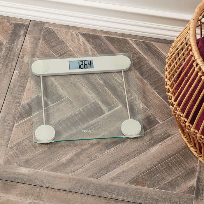 Taylor digital glass scale on a wood floor beside a wicker basket with the display reading 126.4 lb