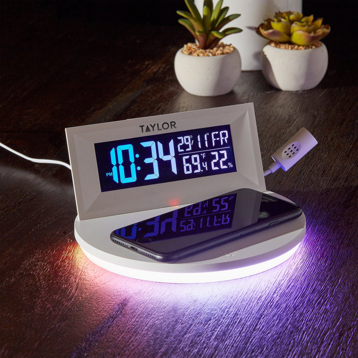 Digital mood light weather station with wireless charging pad on a dark wood desk, with two white succulents in the background
