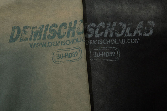 Close-up comparison of olive and black shirt chest graphics with distressed lettering and website text
