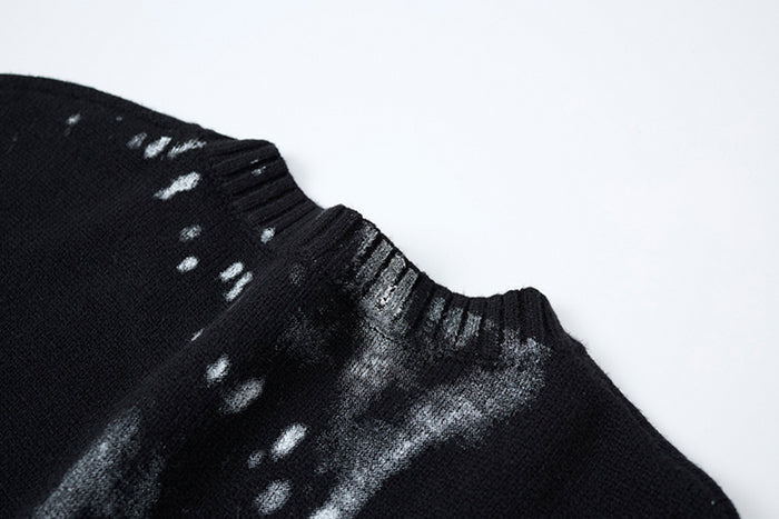 Close-up of the black knit sweater shoulder and ribbed neckline with distressed gray and white marks