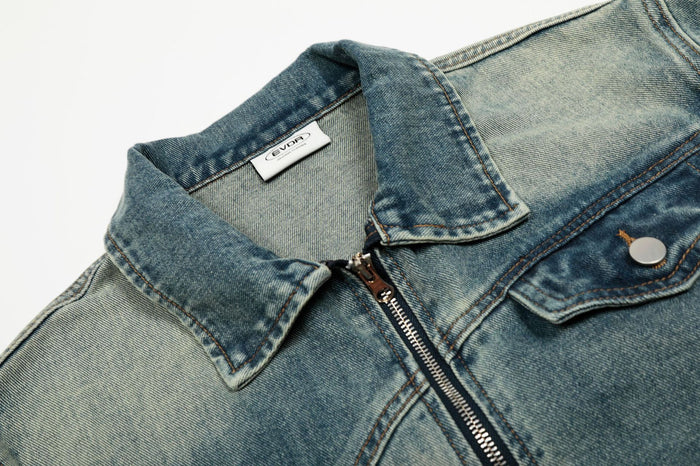 Close-up of the denim jacket collar, metal front zipper, chest flap pocket and contrasting distressed wash
