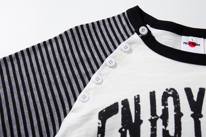Detail of white raglan shirt shoulder with black-and-gray striped sleeve, black collar trim and white buttons