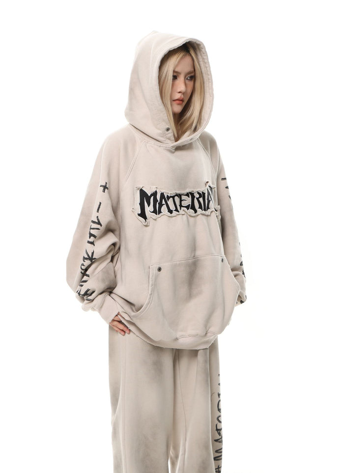 Model wearing a washed beige oversized hoodie with hood up, graphic chest lettering, sleeve print, and matching pants