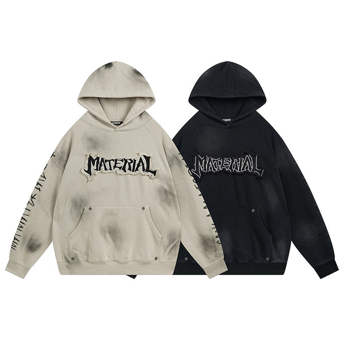 Front view of washed beige and black oversized hoodies with chest lettering, sleeve graphics, and kangaroo pockets