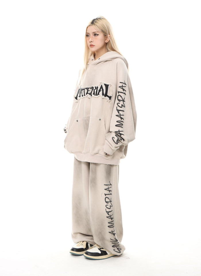 Side model view of a washed beige oversized hoodie with chest lettering, sleeve graphics, and matching printed pants