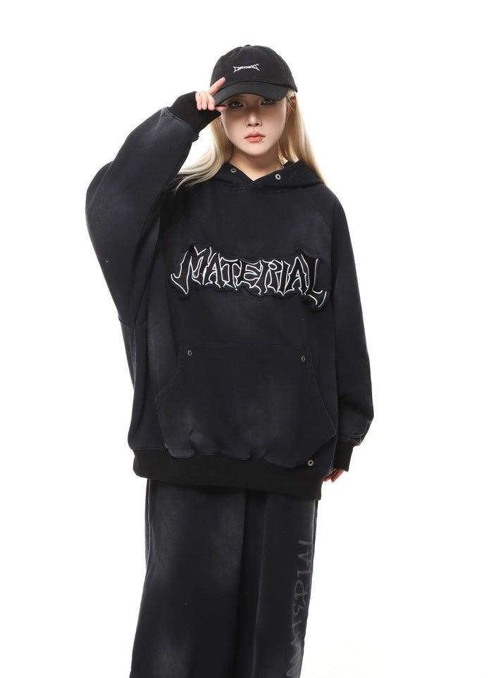 Model wearing a black oversized hoodie with white chest lettering, kangaroo pocket, and matching pants
