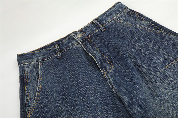 Close-up of blue denim jeans waist showing belt loops, button closure, fly, and front pocket opening