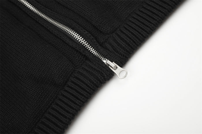 Close-up of the silver zipper slider beside the ribbed lower hem of the black knit jacket