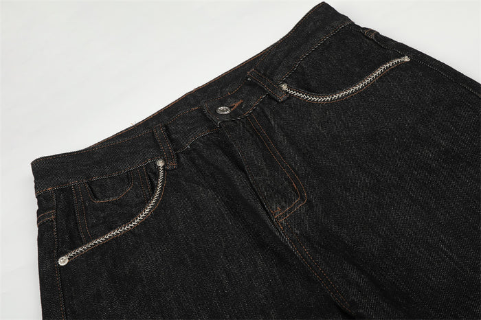 Close-up of black denim jeans waistband, button fly, and curved front pockets with white braided trim