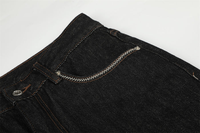 Detailed view of a black denim front pocket with contrasting white braided edging and orange stitching
