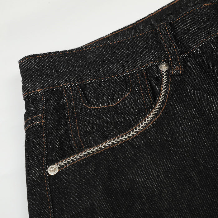 Close-up of a black denim front pocket featuring a curved white braided trim and metal rivet