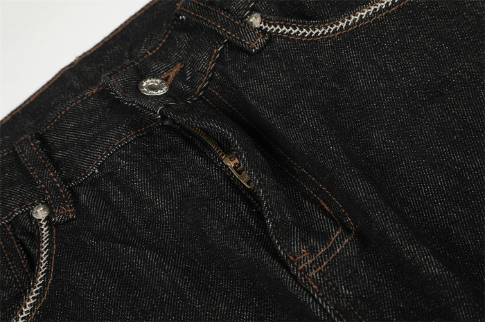 Black denim jeans fly detail showing the metal button, zipper, belt loop, and contrasting stitching