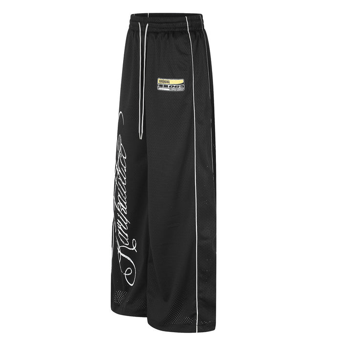 Angled front view of black wide-leg mesh pants with white piping, drawstring waist and partial script graphic