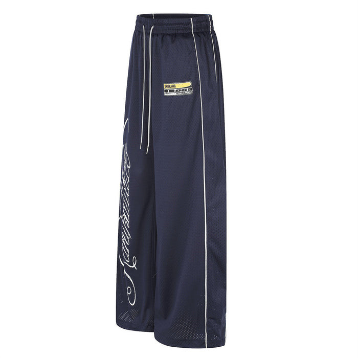 Angled side view of navy wide-leg mesh pants showing white piping, drawstrings and partial script graphic