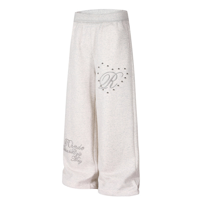 Light gray wide-leg sweatpants angled front view showing embroidered leg graphics and silver studs