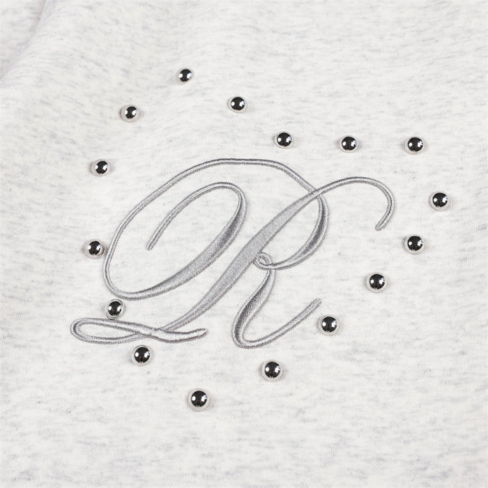 Close-up of raised script embroidery surrounded by small silver studs on light gray sweatpants
