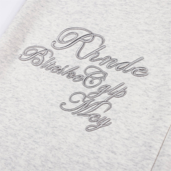 Close-up of ornate raised script embroidery in gray thread on the light gray sweatpants leg