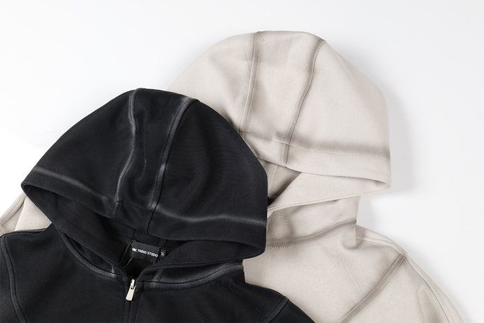 Close-up of overlapping black and light beige hoodie hoods with visible panel seams and front zippers