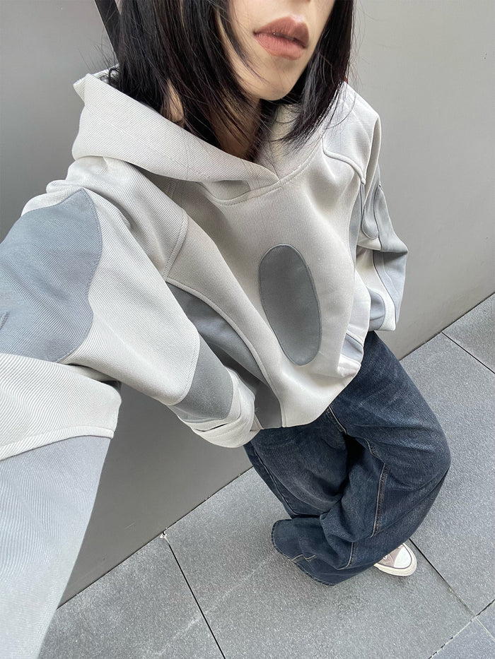 Close model view showing the hoodie’s light gray hood, gray sleeve panels, and oval front patch