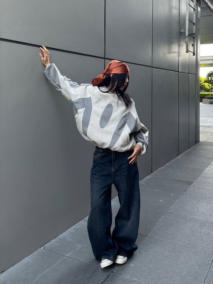 Model posing in a light gray patchwork hoodie with darker gray panels, hood, and ribbed cuffs