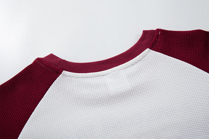 Close-up of the burgundy ribbed raglan neckline joining the white waffle-textured shirt body