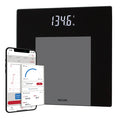 Person stands on a black weight tracking scale with weight shown on the display and a phone screen with metrics.