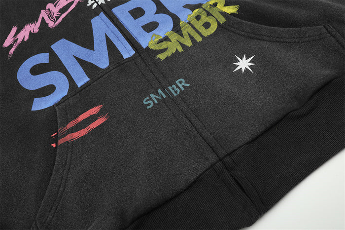 Lower front detail of the black hoodie showing colorful graphics, white star, and ribbed hem
