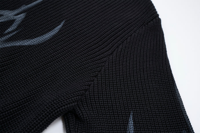 Close-up of the black sweater's textured knit, side seam, and partial gray flame graphic on the sleeve