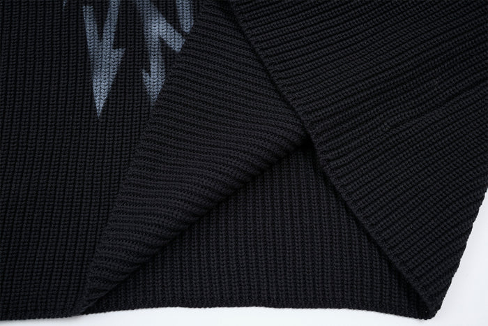 Close-up of the black sweater's ribbed lower hem and textured knit body with a partial gray graphic