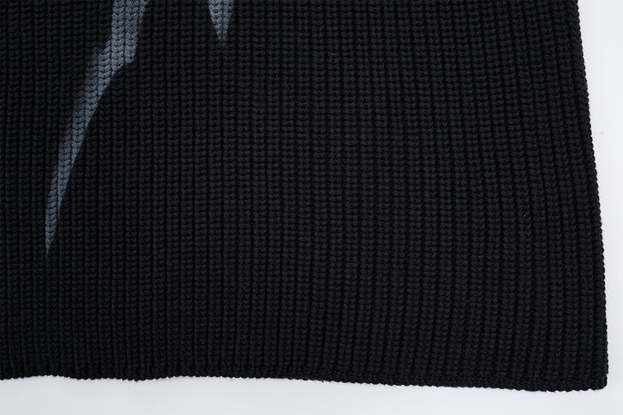 Close-up of the black sweater's textured knit body and ribbed bottom hem with a partial gray flame graphic