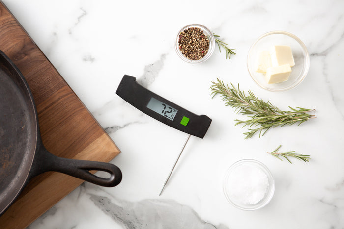 Green TruTemp Ultra-Fast Thermometer with stainless steel probe on a marble counter beside a skillet and rosemary sprigs