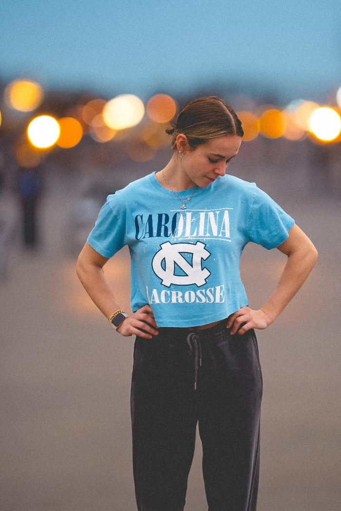 on model: Blue Tshirt frontal view saying Carolina Lacrosse in Navy Blue & White Lettering with paint splattering