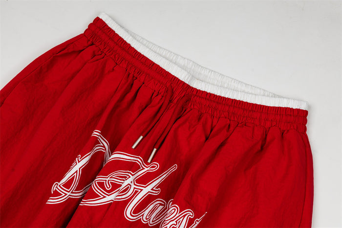Close-up of red pants showing the elastic double waistband, drawstring, and partial white script embroidery