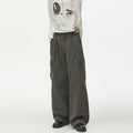 Army green wide-leg cargo pants worn from the front, showing pleats, side pockets, and oversized trouser legs