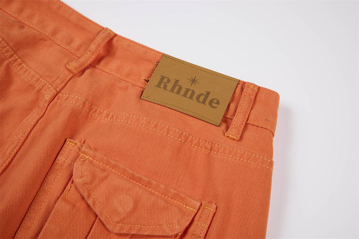 Close-up of the orange waistband showing belt loops, back pocket flap, and rectangular branded label