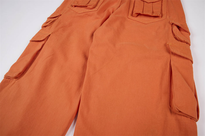 Close-up of orange wide-leg cargo pants showing layered flap pockets along both outer legs
