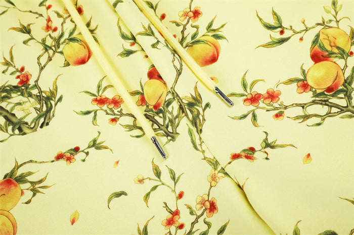 Close-up of pale yellow fabric showing peach blossoms, fruiting branches, and cream drawstring ends