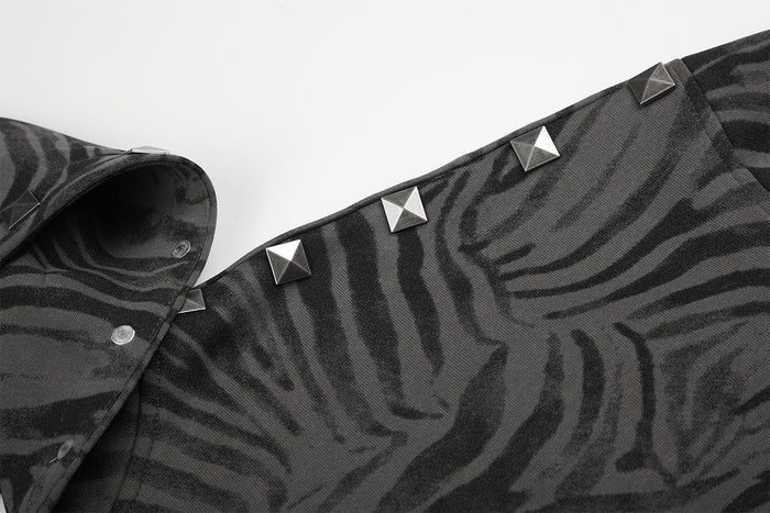 Close-up of pyramid studs along the shoulder seam of a grey zebra-print hoodie jacket