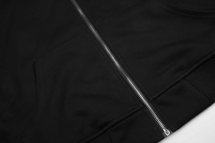 Close-up of the black hoodie’s lower front showing the metal zipper, seam, and front pocket edge