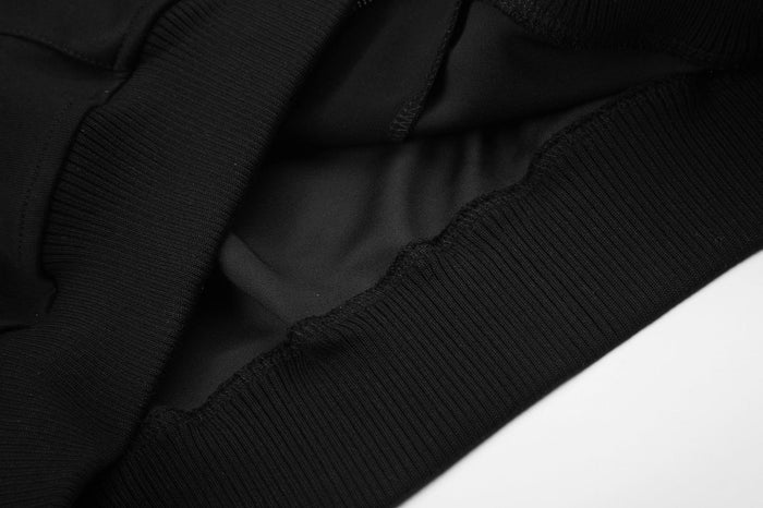 Close-up of black hoodie construction showing overlapping fabric panels, stitching, and a ribbed lower edge